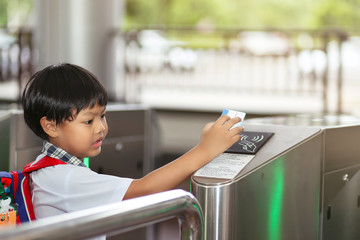 An Asian young schoolboy holding a keycard at pedestrian access control flap barriers in a school.