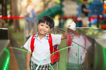 An Asian young schoolboy holding a keycard at pedestrian access control flap barriers in a school.