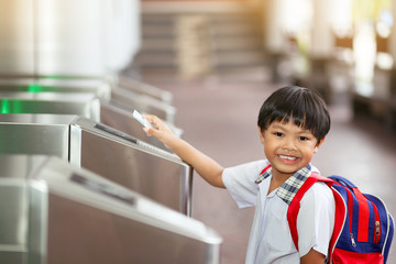 An Asian young schoolboy holding a keycard at pedestrian access control flap barriers in a school.