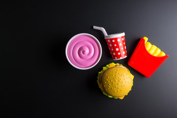 Plastic burger, French fries Fast food on black background. Children's toy. Concept of harmful artificial food. Plastic. Not organic. Not useful.