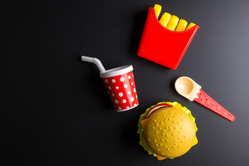 Plastic burger, French fries Fast food on black background. Children's toy. Concept of harmful artificial food. Plastic. Not organic. Not useful.