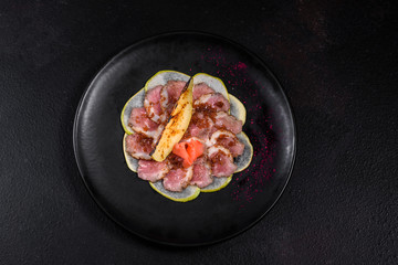 Edged pieces with caramelized pear on a black ceramic plate. Baked meat sliced with thin pieces