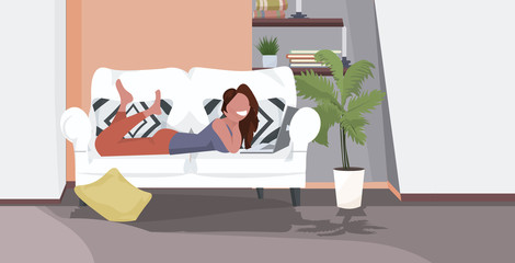 girl lying on sofa using laptop happy woman relaxing at home modern living room interior horizontal full length flat