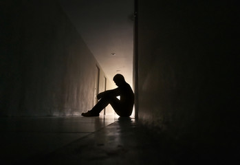 Silhouette of depressed man sitting on walkway of residence building. Sad man, Cry, drama, lonely and unhappy concept.