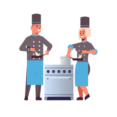 cooks couple professional chefs using frying pan stirring food man woman restaurant kitchen workers in uniform standing together near stove cooking concept flat full length