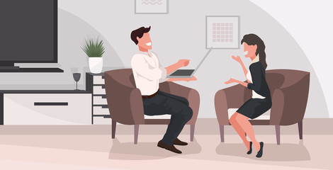 man woman sitting on armchair relaxing at home couple having fun using laptop and discussing together modern living room interior flat full length horizontal