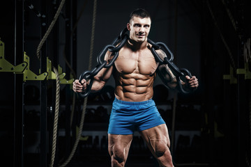 Fototapeta na wymiar Muscular man bodybuilder training in gym with iron chain and posing. Fit muscle guy workout with weights and barbell