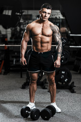 Fototapeta na wymiar Muscular tattoo man bodybuilder training in gym and posing. Fit muscle guy workout with weights and barbell