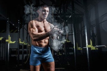 Fototapeta na wymiar Athletic pumped man bodybuilder slaps magnesia in gym
