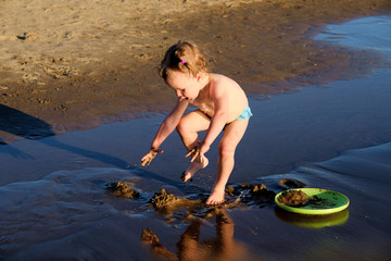Baby boy plays by the water in the sand.