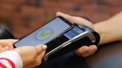 Hand of young woman pays for purchases using the contactless payment nfs system - Powered by Adobe