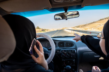 Two arabic women driving a car while one is talking on the phone