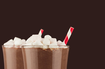 Elegant hot chocolate with marshmallows and red striped straw closeup, details, top section on dark brown background, copy space.