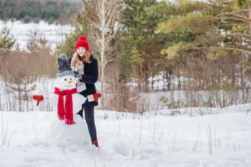 Naklejka premium happy teenager girl with snowman in winter forest