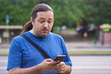 Adult man with a cigarette suspiciously looks at the screen of a mobile phone on a city street