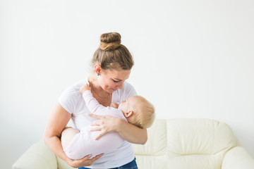 Young happy loving mother holding her baby daughter in her arms against the window. Maternal care. Childcare.