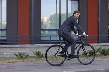 Fototapeta premium Handsome young businessman riding on his bicycle in the city. Ecologic transport concept. 