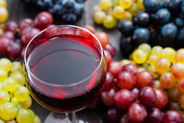 glass of red wine and grapes on black wooden table background