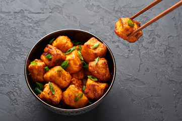 Paneer Manchurian or Paneer 65 in bowl at black concrete background. Paneer Manchurian is Indian Chinese cuisine dish with panner cheese, tomatoes, onion, soy sauce. Copy space