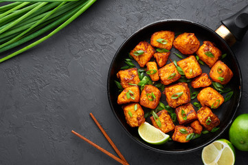 Paneer Manchurian or Paneer 65 in pan at black concrete background. Paneer Manchurian is Indian Chinese cuisine dish with panner cheese, tomatoes, onion, soy sauce. Copy space