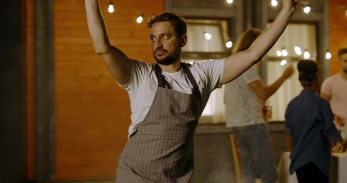 Caucasian male silly dancing while cooking barbecue with friends outdoors. 4K UHD