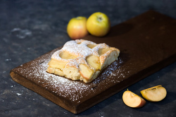 a piece of Apple pie on a wooden Board in powdered sugar on a dark background