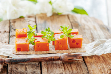 Delicacies, spicy cheeses. Red cheddar, on a beautiful textured wooden background with twigs of savory is a savory snack for gourmets. Selective focus