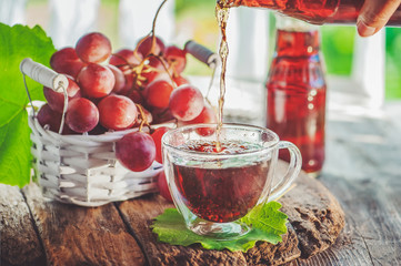 Grape juice pours from the bottle into a glass Cup. Bunch of grapes in a white wicker basket. Grape juice in a clear bottle