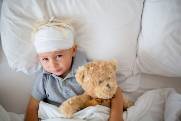 Little toddler boy with head injury, lying in bed, tired