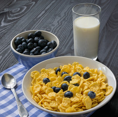 Morning breakfast. Plate of cornflakes with blueberries and a glass of milk on a dark wooden background