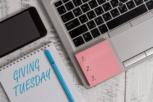 Writing note showing Giving Tuesday. Business concept for international day of charitable giving Hashtag activism Laptop ruled notepad smartphone sticky note on wooden table