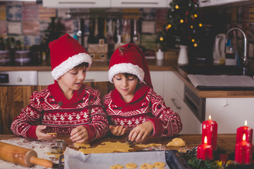 Sweet toddler child and his older brother, boys, helping mommy preparing Christmas cookies at home .