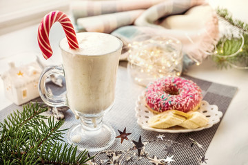 Irish traditional winter cream cocktail eggnog in a glass mug with milk, rum and cinnamon, banana covered with whipped cream, Christmas decorations. Natural smoothies