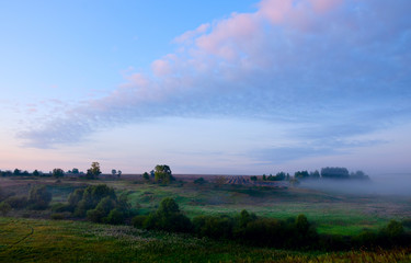 Tranquil hazy landscape with green trees and hills covered by morning fog