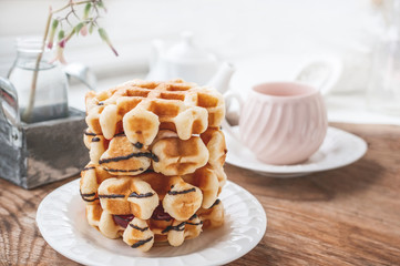 Fresh round Belgian waffles with a layer of jam poured with chocolate on a white plate with a Cup of tea. Close up