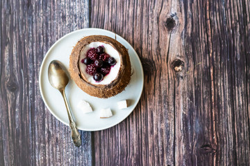 Berry dessert with yogurt in a cup of coconut on a wooden background. Blackberries, raspberries, blueberries, black currants.