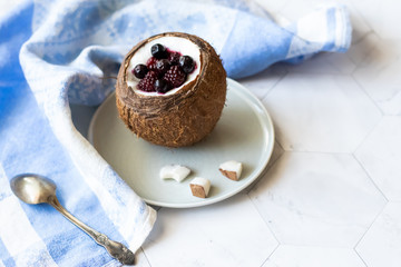 Berry dessert with yogurt in a cup of coconut on a light background. Blackberries, raspberries, blueberries, black currants. Blue napkin