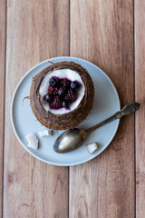Berry dessert with yogurt in a cup of coconut on a wooden background. Blackberries, raspberries, blueberries, black currants.
