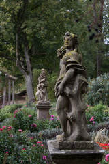Fototapeta premium An old statue of a goddess stands in a botanical garden in Rothenburg ob der Tauber, covered with green moss, among the flowers.