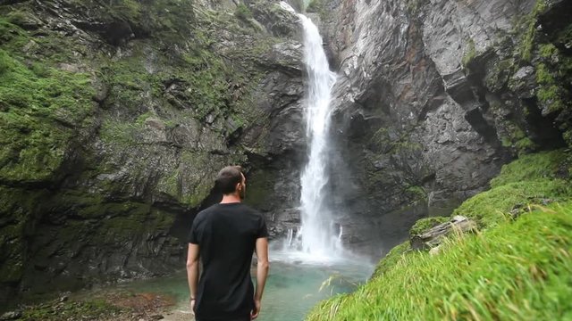 Young man admires a waterfall and feels the energy of nature around him.