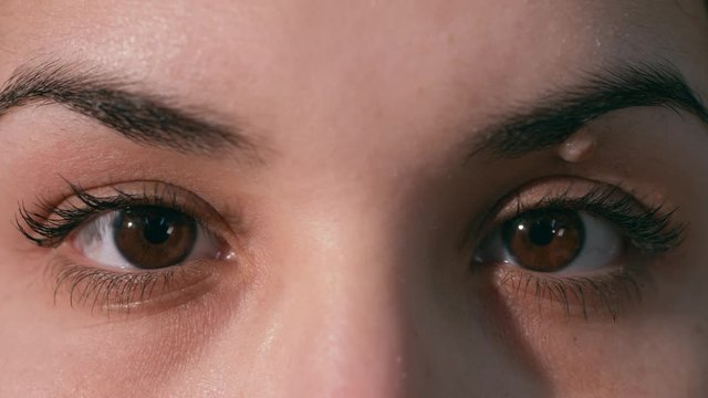 Young woman opens her eyes quickly and looks at camera. Brown eyes, wart in the eye. Close-up shot