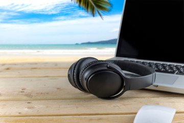 Obraz na płótnie Canvas Headphones and laptop on wood table with beach background. With copy space for text or design. Technology concept.