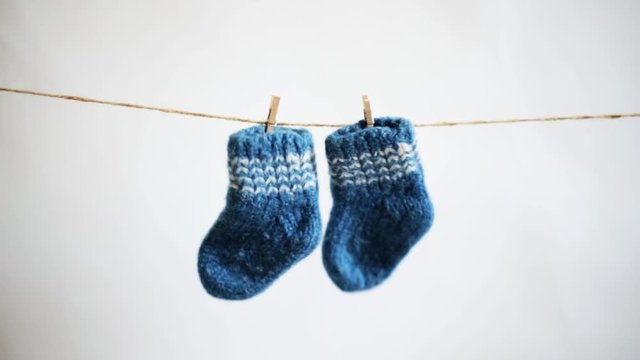blue knitted woolen baby socks hanging on a rope with clothespins on a white background. baby expectation concept - Powered by Adobe
