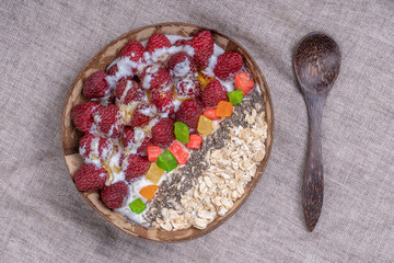 Smoothie in coconut bowl with raspberries, oatmeal, candied fruit and chia seeds for breakfast , close up. The concept of healthy eating, superfood