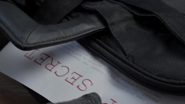 Black glove pulling top secret document containing classified information out of briefcase