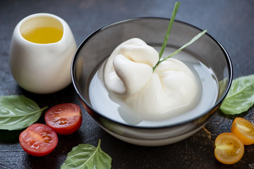 Closeup of a bowl with burrata cheese on a brown stone surface, horizontal shot, selective focus
