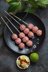 Fresh uncooked nem nuong or vietnamese pork meatballs on skewers. Flatlay on a dark grey stone background