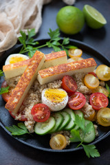 Quinoa with roasted cheese, vegetables and eggs on a metal serving tray, close-up, vertical shot