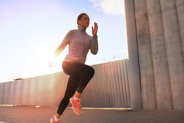 Young attractive sporty fitness woman running while exercising outdoors at sunset or sunrise in city