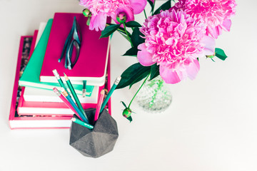 bouquet of pink peonies, a stack of books, pencils and a notebook on a white table, top view.